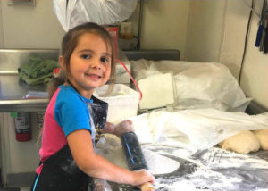Sierra, the youngest member of the Serrianni family, rolling out pizza dough and smiling for the camera