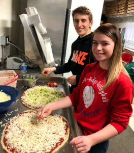 Bradley and Isabella, young members of the Serrianni family, smiling and making pizzas
