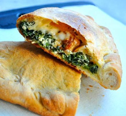 An image of a spinach with white sauce ham, and provolone cheese calzone, it's cut in half to expose the beautifully baked center.