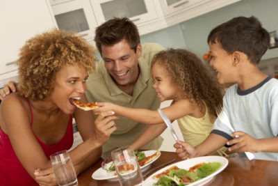 An image of a multi-racial family eating pizza at Serrianni's. There are 2 children and everyone is smiling and look very happy.