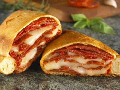 An image of a pepperoni and mozarella cheese calzone, it's cut in half to expose the beautifully baked center.