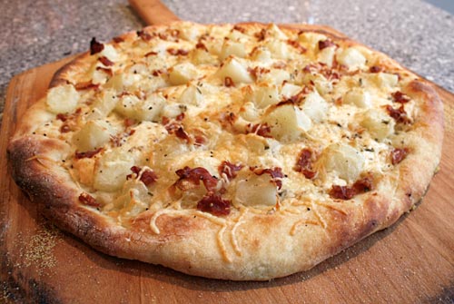 image 2 of a potato pizza, it has thinly sliced potato rounds, cheese and some oregano sprinkled on top. 