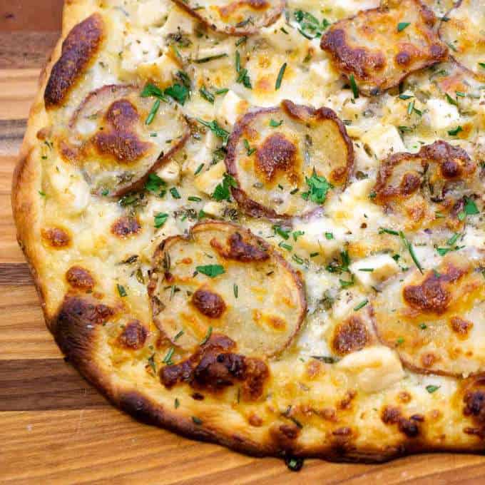 An Image of a potato pizza, it has thinly sliced potato rounds, cheese and some oregano.