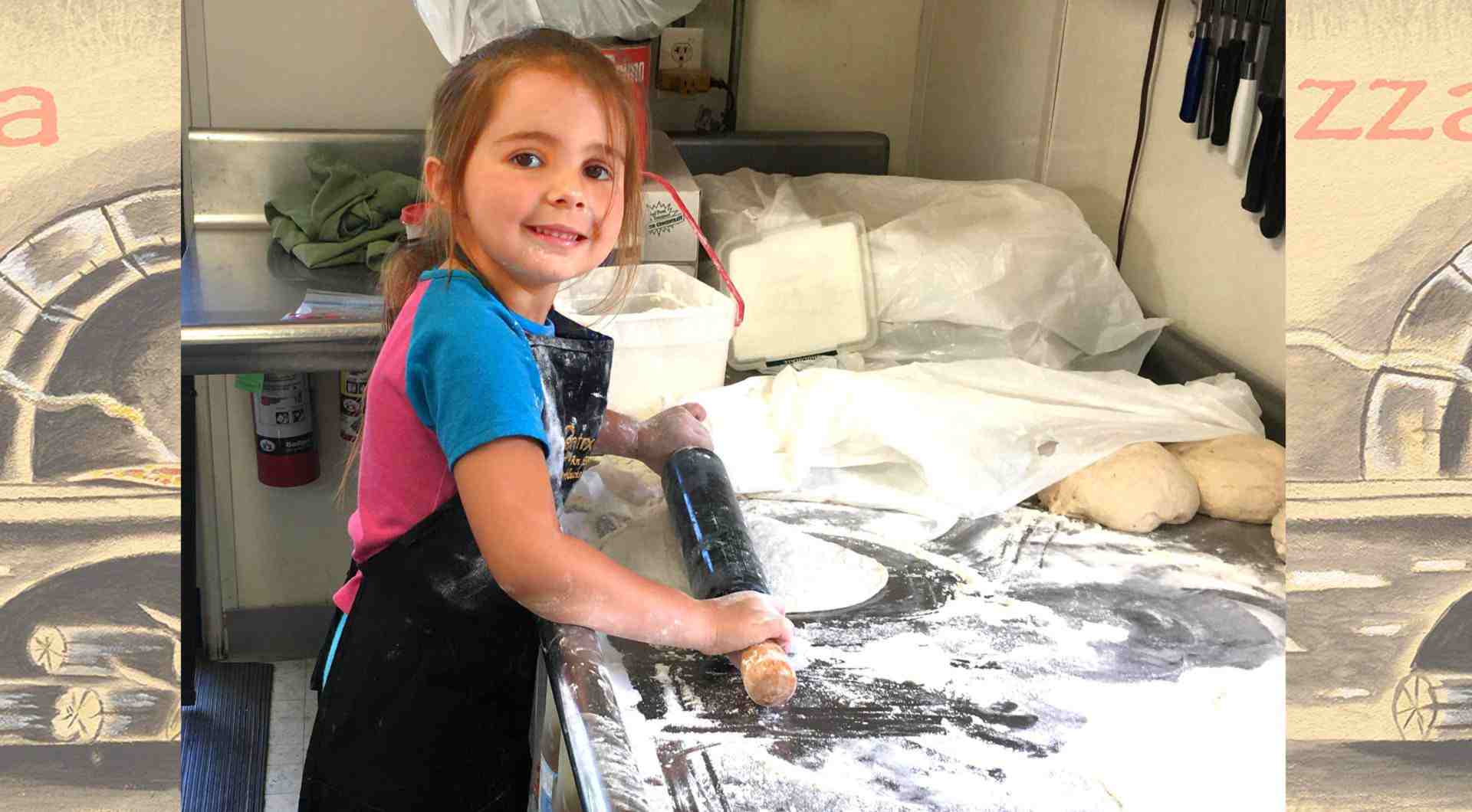 an image of the grand daughter of the owner Val, she is rolling out some pizza dough, standing on a stool, she looks to be about 5 years old, it's a very cute picture